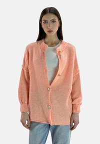 Cardigan lavorato a maglia color pesco con scollo tondo, vestibilità oversize, maniche lunghe e tre bottoni decorativi sul davanti.