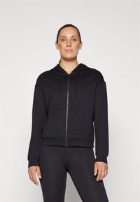 Black zip-up hoodie made of soft fabric, featuring a front pocket, drawstring hood, and ribbed cuffs and hem. Paired with black leggings.