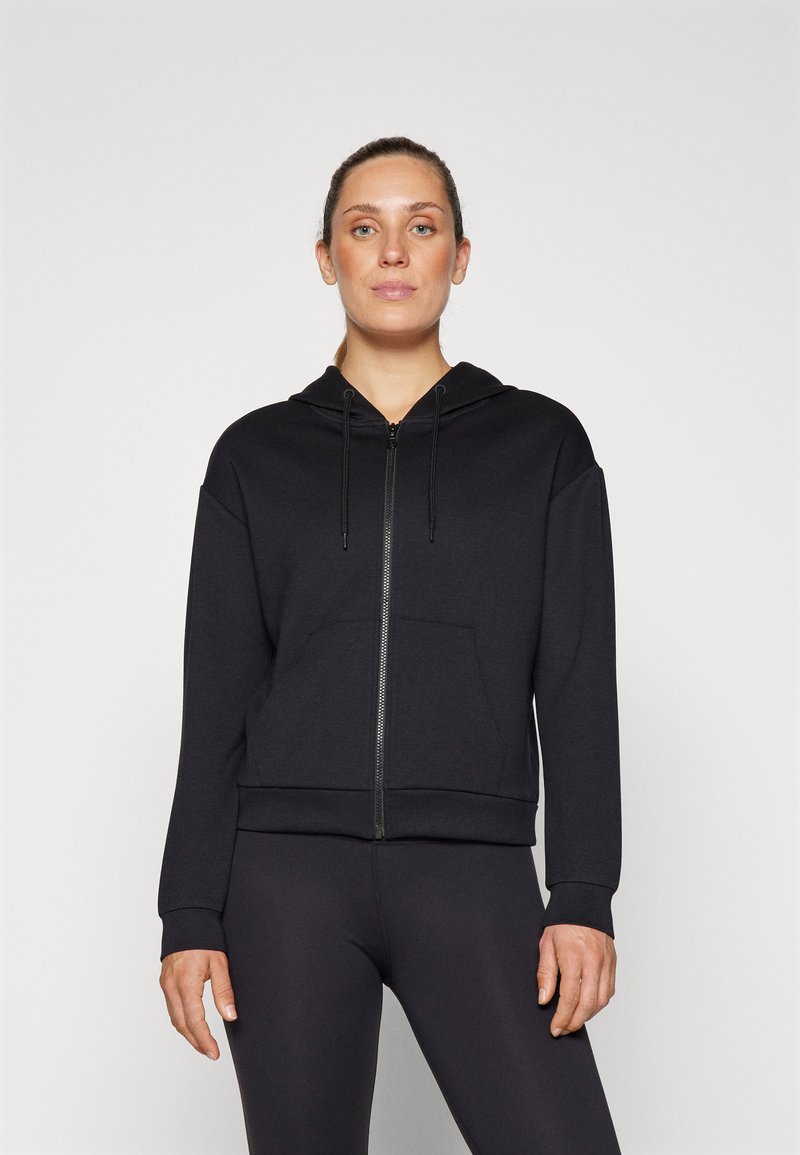 Black zip-up hoodie made of soft fabric, featuring a front pocket, drawstring hood, and ribbed cuffs and hem. Paired with black leggings.