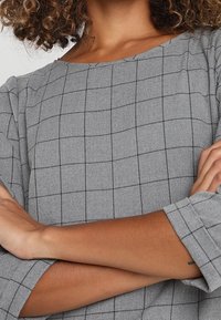 Top gris con un diseño a cuadros, con un escote ancho y mangas tres cuartos. Tejido suave con una textura sutil.