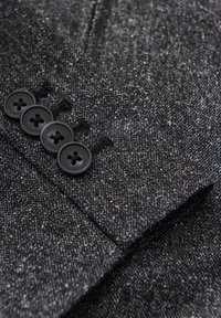 Tissu texturé gris foncé avec quatre boutons noirs cousus de près en ligne sur le poignet d'une manche de veste.