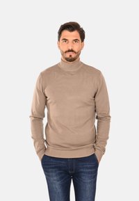 Maglione beige a collo alto in tessuto a maglia coste, maniche lunghe, vestibilità aderente, abbinato a jeans denim blu scuro.