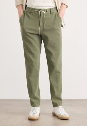 Pantalons en velours côtelé verts avec une coupe décontractée, taille élastique avec cordon de serrage, poches latérales et associés à des baskets blanches sur un fond neutre.