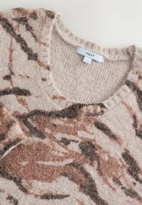 Jersey de punto en suave beige con patrones abstractos en marrón y óxido. Presenta un cuello redondo y una tela texturizada. Etiqueta de la marca visible.