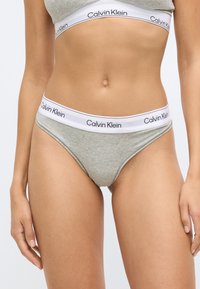 Ανοιχτό γκρι βαμβακερό σλιπ με λευκή μέση που φέρει μαύρο λογότυπο "Calvin Klein". Ομαλή υφή, χαμηλή μέση και ελάχιστη κάλυψη.