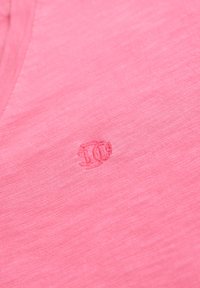 Chemise rose à manches courtes avec une texture subtile, ornée d'un petit logo brodé dans une teinte assortie sur le côté inférieur gauche.