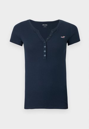 T-shirt bleu marine à manches courtes, texture côtelée, col en V avec patte de boutonnage à cinq boutons, avec un petit logo rouge sur le côté gauche de la poitrine.