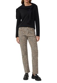 Maglia nera a maniche lunghe con collo drappeggiato e dettaglio con cravatta, abbinata a jeans beige con stampa leopardata e mocassini neri chunky.