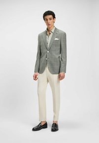 Grårutig kavaj med två knappar, kombinerad med en ljusbeige skjorta, beige byxor och svarta loafers. Slät textur och skräddarsydd passform.