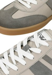 Beige en grijze suède sneakers met witte veters en rubberen gumzolen, voorzien van gestikte panelen en een logo op de tong.
