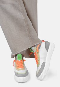Sneakers bianchi e grigi con un design intrecciato verde e arancione testurizzato, dotati di lacci brillanti e suole in gomma prominenti.
