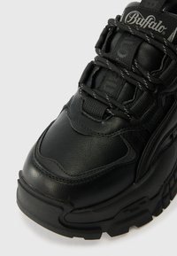 Adidasi negri cu un superior din piele texturată, sistem de șireturi proeminent și o talpă groasă din cauciuc. Include branding pe limbă.