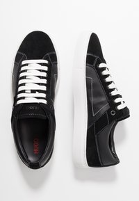 Sneaker nere in camoscio e pelle sintetica con lacci bianchi, suola bianca e cuciture a contrasto. Presenta il logo sulla linguetta.