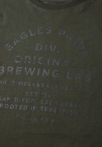 Olive-green t-shirt wykonany z miękkiego materiału z wyblakłym niebieskim napisem szczegółowo opisującym laboratorium warzelne, z prążkowanym okrągłym dekoltem i luźnym krojem.