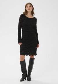 Rochie din dantelă neagră cu mâneci lungi și tiv ondulat, asortată cu cizme de piele negre până la genunchi. Textură netedă, model elegant.
