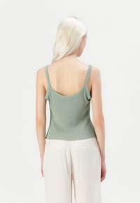 Top a maniche sottili di colore verde chiaro con una lavorazione a coste e schiena scoperta. Il tessuto appare morbido, aderente al corpo, con un design senza cuciture.