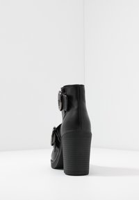 Schwarze, hochhackige Knöchelboots aus Leder mit runder Zehenpartie, großer runder Schnallenakzent und strukturiertem Gummisohle.