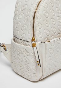 Borsa in pelle color crema con motivo a logo in rilievo e dettaglio della cerniera dorata su sfondo bianco.