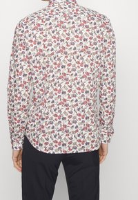 Camisa de manga larga floral en blanco con patrones de flores en rojo y azul marino. Cuello estándar y puños con botones, hecha de tejido ligero.