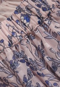 Lys pink stof med samlede sømme præsenterer et blomstermønster i blå og lilla nuancer, som fremhæver fine detaljer og teksturer.
