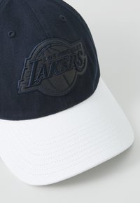 Navy blue cap with a white brim, featuring a dark embroidered "Los Angeles Lakers" logo on the front. Cotton material with smooth texture.