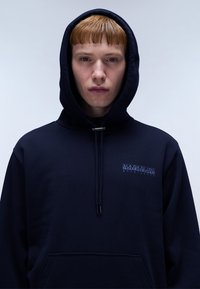Marineblauwe hoodie van katoen, met een voorkantzak, een trekkoordcapuchon en een subtiele merkl logo op de borst. Zachte textuur.