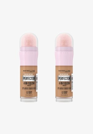 Maquillage Perfecting 4-en-1 Glow de Maybelline dans deux tubes identiques, avec des bouchons roses, des dessus transparents et une teinte caramel moyen.