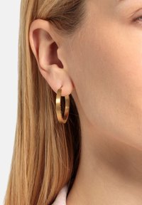 Pendientes de aro de oro con un acabado pulido, que presentan un diseño circular grueso. Los pendientes cuelgan de un cierre delgado.