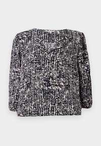 Marinebluse med et strukturert, prikkete mønster i krem og beige, med V-hals og lange puffermer. Laget av lett stoff.