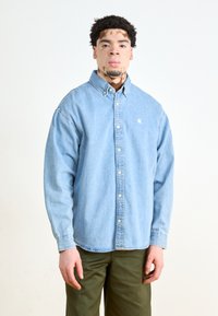 Lichtblauw denim overhemd met button-down kraag, witte knopen en een klein logo. G Combineert met olijfgroene broek. Soepele textuur.