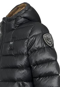 Sort pufferjakke med hætte og en glansfuld overflade. Har stikninger, et logo-patch på ærmet, og en kontrastfyldt brun foret.