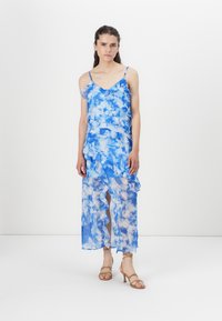 Ελαφριά μπλε φόρεμα tie-dye με στρώσεις από ρίγες, τιράντες spaghetti και διαφανή φινίρισμα, με σκίσιμο στο γόνατο.