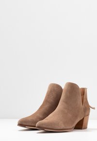 Tan suède enkellaarsjes met een spitse neus, een lage blokhak en open zijuitsparingen. Heeft een subtiele textuur en gestikte details.