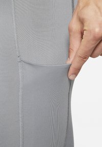 Grå treningsleggings med en teksturert overflate, som har en sidelomme og kontrasterende flatlock-søm detaljer.