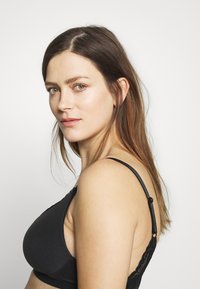 Sutiã preto com detalhes em renda, tecido suave e alças ajustáveis. Apresenta um design liso e possui uma forma arredondada.