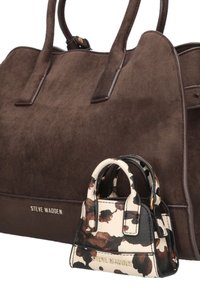 Bruine suède handtas met twee handvatten, gecombineerd met een kleine zwart-wit gevlekte leren tas, beiden met het logo "Steve Madden."