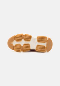 Gummisåle til sneakers med mønstrede rifler, med et beige ytre lag og en hvit mellomsåle. Inneholder logo-detaljering i midten.