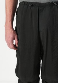 Shorts légers noirs en tissu texturé, avec une taille élastique et un cordon de serrage. Possède des poches latérales et une coupe ample.