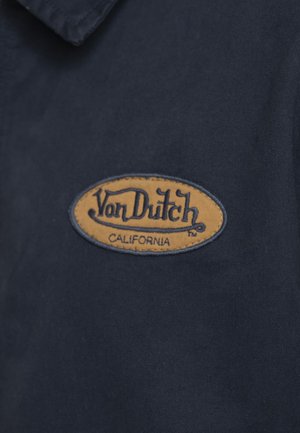 Écusson du logo Von Dutch California en fil orange et noir sur tissu bleu foncé.
