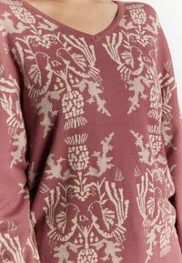 Maglione rosa con scollatura a V, motivo floreale intrecciato in crema, caratterizzato da una texture morbida e una vestibilità comoda.