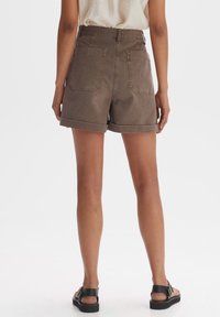 Bruine denim shorts met een hoge taille, opgerolde zoom en twee achterzakken, gecombineerd met zwarte sandalen. De stof heeft een gladde textuur.
