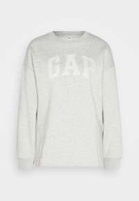 Jasnoszary sweatshirt z prążkowanymi mankietami i okrągłym dekoltem. Z przodu znajduje się napis "GAP" w wyraźnych, białych literach. Miękka tekstura.