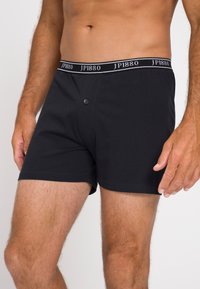 Boxer shorts de algodón negro con una cinturilla suave que presenta el nombre de la marca "JP1880." Cierre frontal con botón y diseño liso y ajustado.