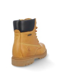 Bota impermeable marrón con un cuello negro, que cuenta con un diseño de cordones, costuras amarillas y una suela de goma robusta.