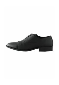 Zapato de vestir de cuero negro con textura suave, punta redondeada y tacón bajo, que cuenta con seis ojetes para los cordones y sutiles detalles de costura.