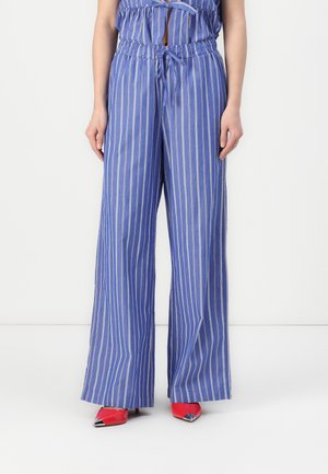 Pantalons larges à rayures bleu et blanc en tissu léger, avec une taille élastique et un cordon de serrage, associés à des talons rouges.
