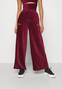 Pantalons larges bourgogne en tissu doux, dotés d'une taille à cordon de serrage et de logos brodés. Associés à des baskets noires pour le contraste.