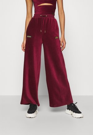 Burgundy vida byxor i mjukt tyg, med resårmidja och broderade logotyper. Parat med svarta sneakers för kontrast.