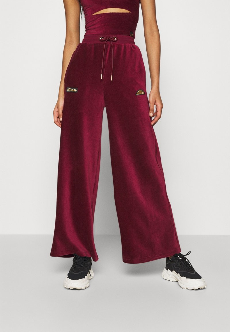 Pantalons larges bourgogne en tissu doux, dotés d'une taille à cordon de serrage et de logos brodés. Associés à des baskets noires pour le contraste.