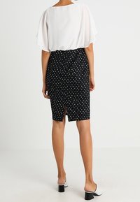 Gonna nera a pois con uno spacco sul retro, abbinata a una blusa bianca trasparente. La blusa presenta maniche corte e fluide e una scollatura rotonda.